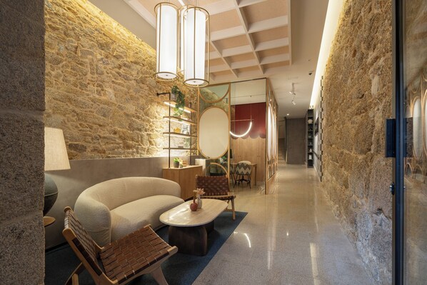A modern interior with a stone wall, a sofa, a wooden chair, a coffee table, and a desk with shelves. - Marina 30 (A Coruña)
