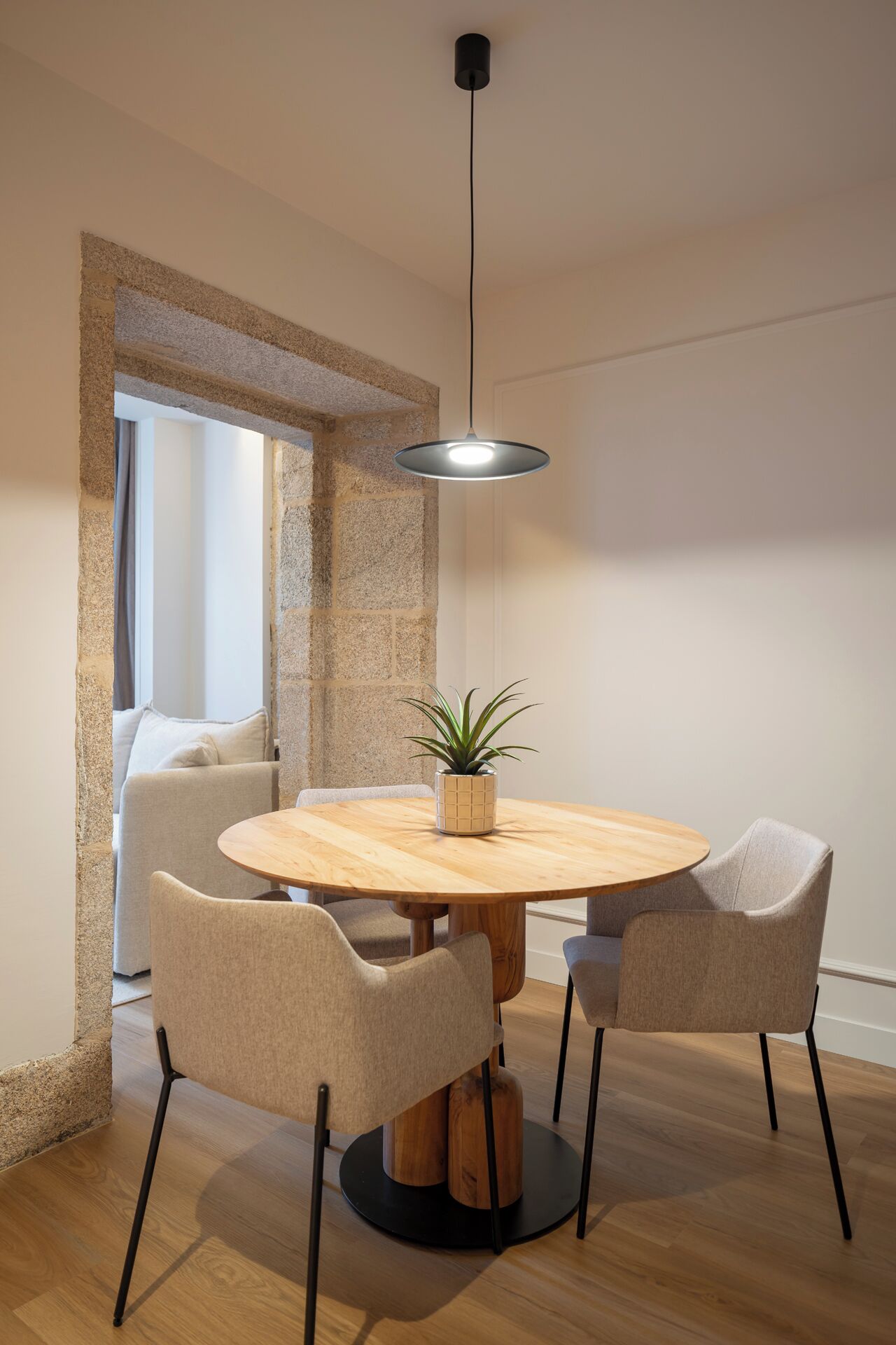 A round wooden dining table with two chairs, a hanging pendant light, and a potted plant.