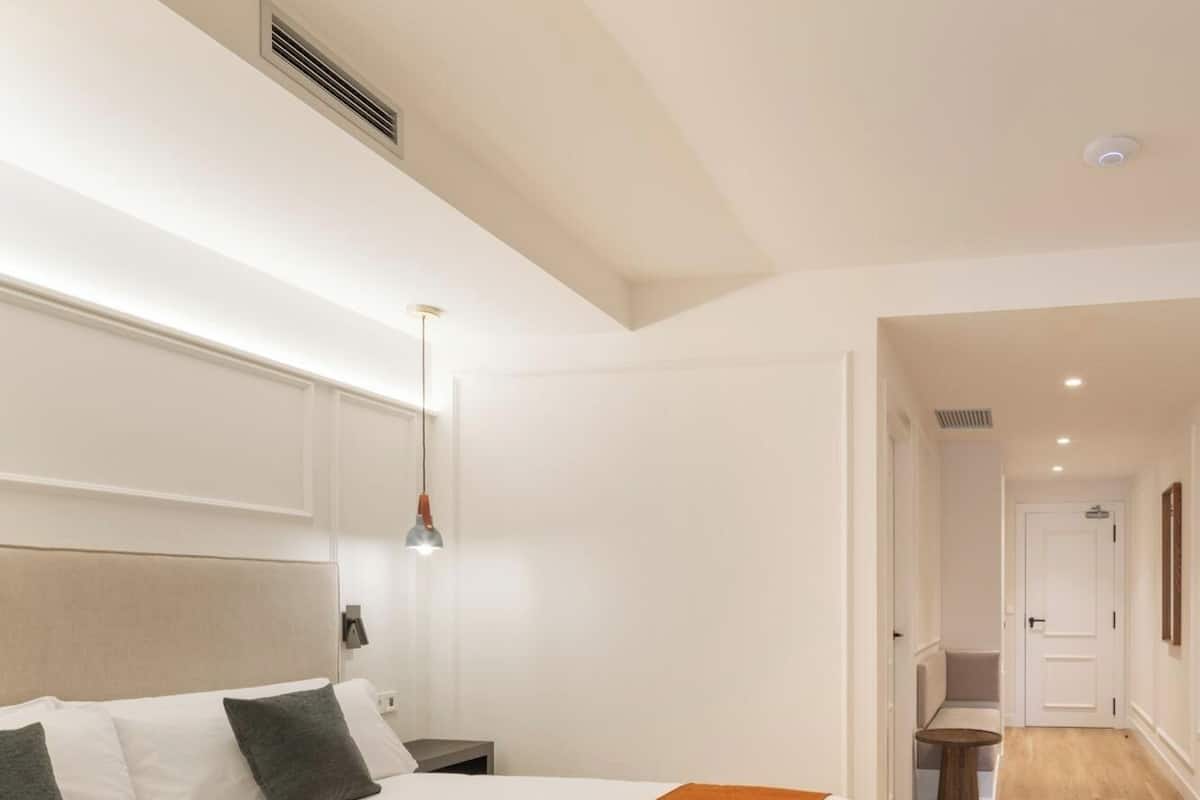 A hotel room with a large bed, a bedside table, a lamp, and a view of the hallway.