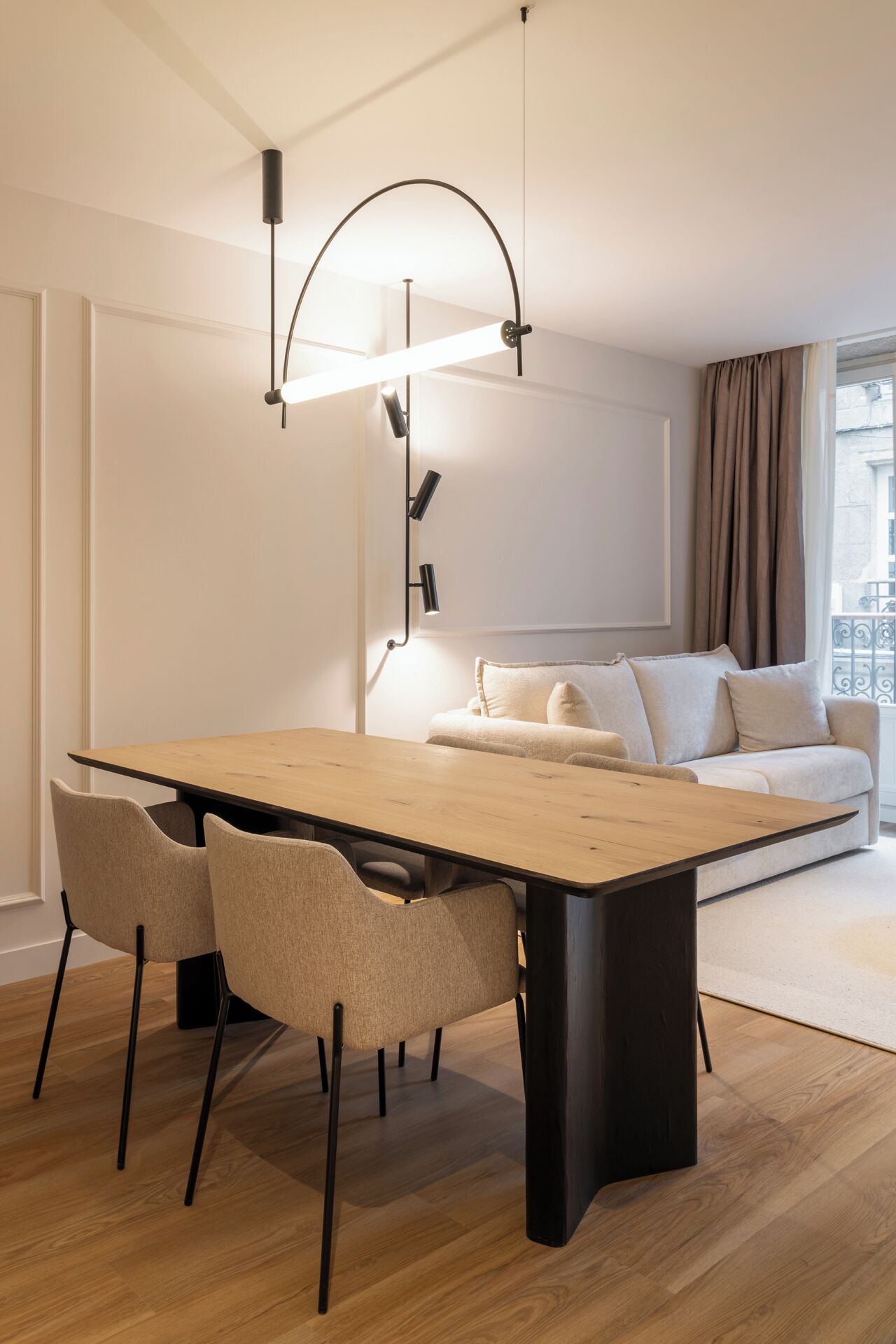 A modern living room with a wooden dining table, two chairs, a sofa, and a floor lamp.