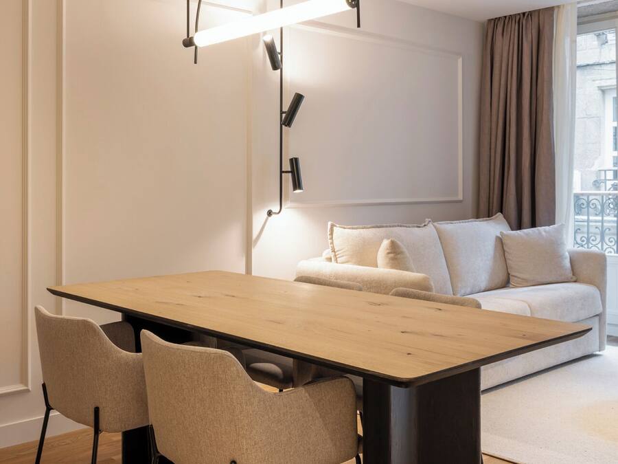 A modern living room with a wooden dining table, two chairs, a sofa, and a floor lamp.
