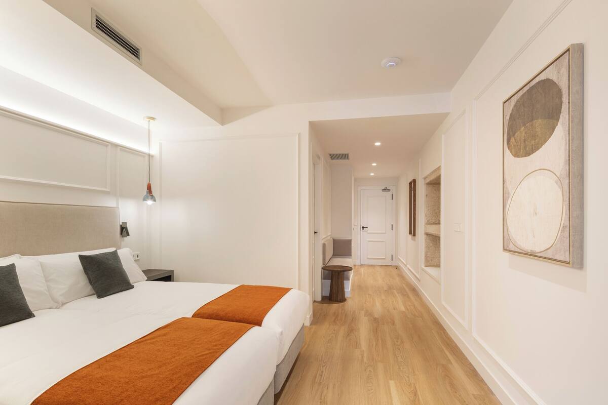 A hotel room with a large bed, a bedside table, a lamp, and a door leading to a hallway.