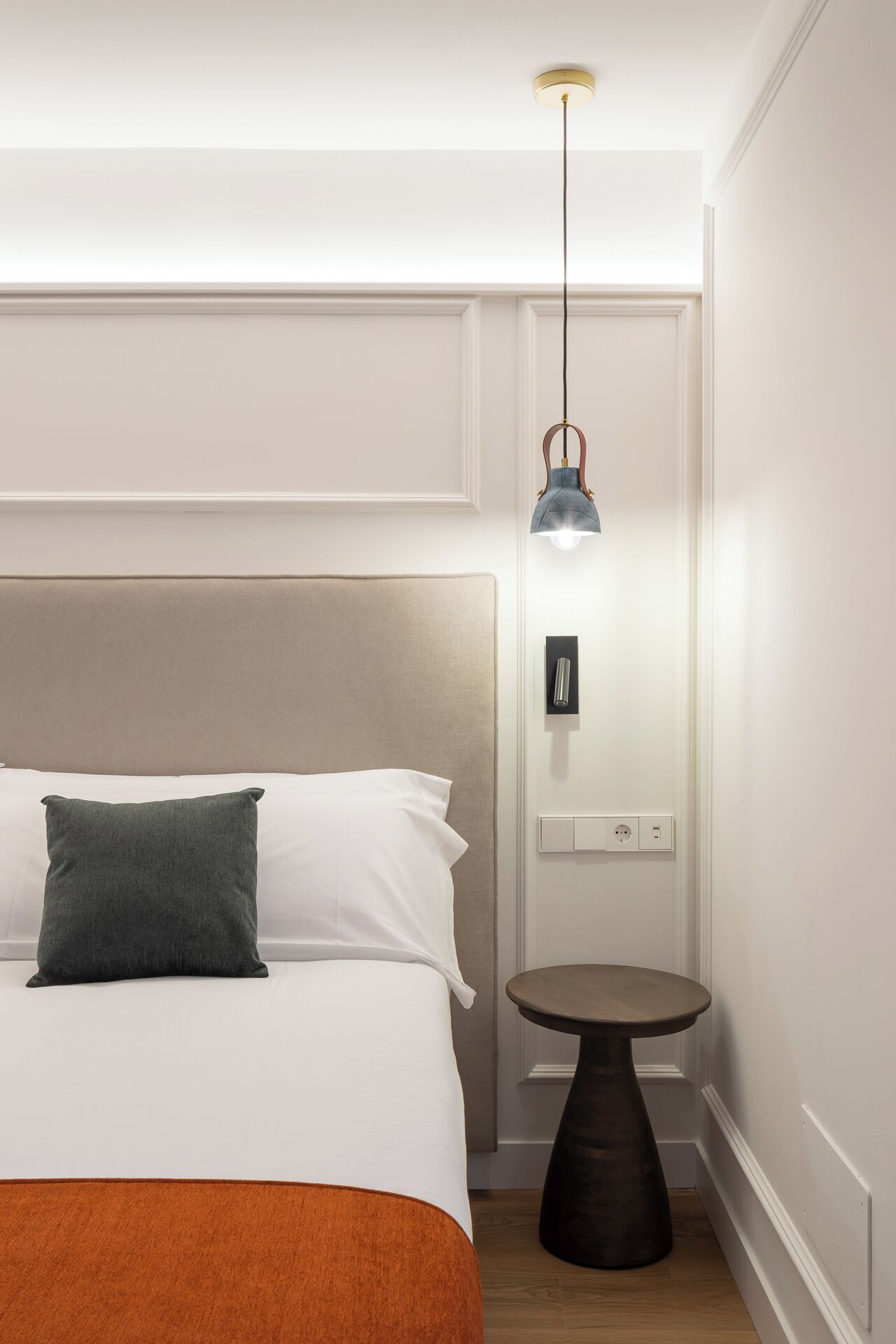 Una habitación de hotel con una cama, una mesita de noche, una lámpara y un interruptor de luz en la pared.