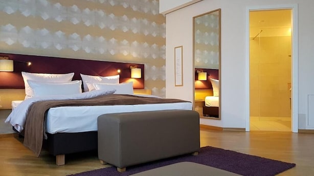 A modern hotel room with a large bed, bedside lamps, a mirror, and a view of the bathroom. - Restaurant & Hotel Einhorn (Oppenweiler)
