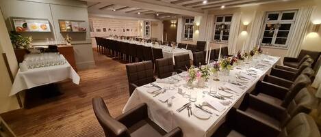Een lange eettafel gedekt voor een formeel evenement, met meerdere stoelen, een buffet en een menukaart.