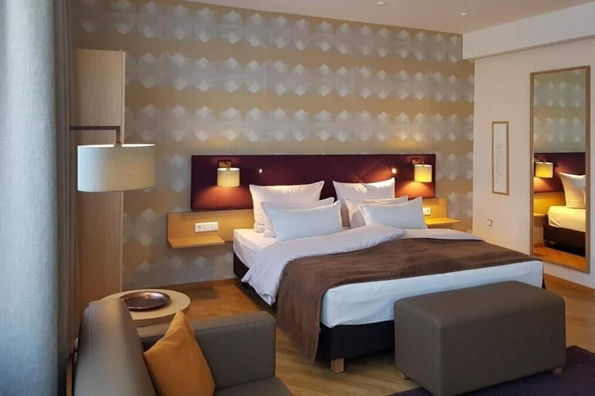 A hotel room with a large bed, two bedside tables with lamps, a sofa, and a mirror.