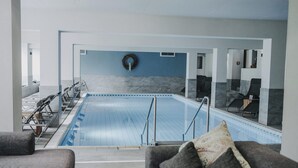 Piscina interior moderna con vista despejada del área, zonas de estar y una fuente en la pared.