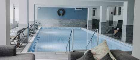 Piscina interior moderna con vista despejada del área, zonas de estar y una fuente en la pared.