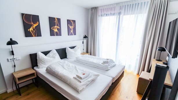 Ein Hotelzimmer mit zwei Betten, einem Schreibtisch, einem Stuhl, einem Fernseher und Bildern an der Wand.
