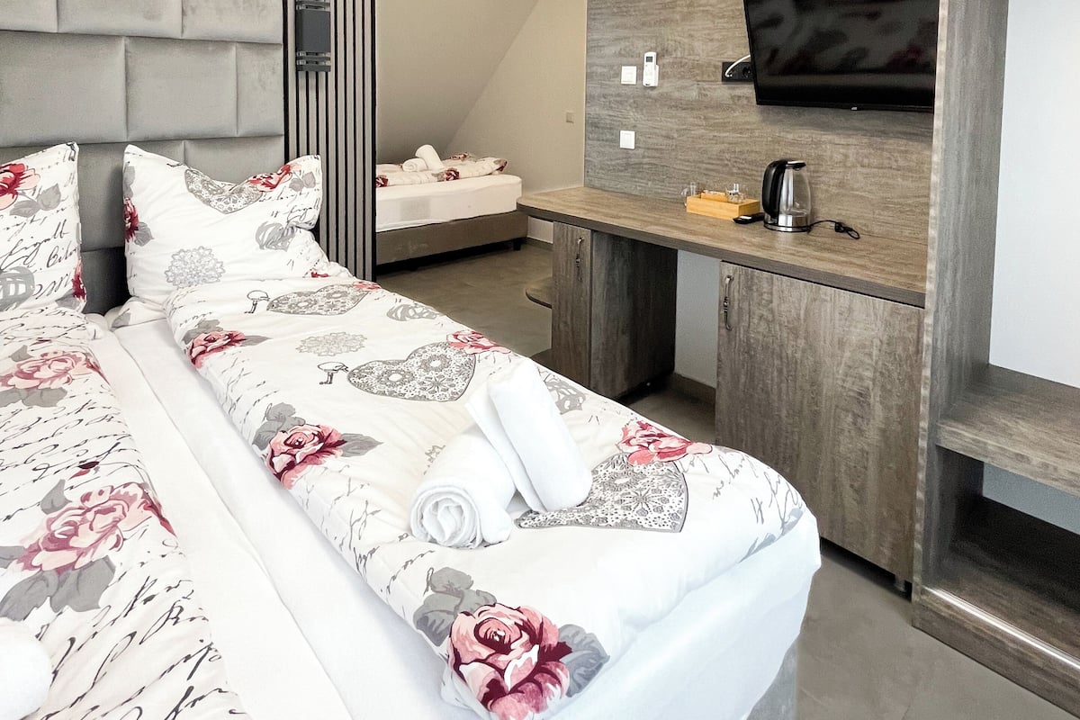 A modern hotel room with a large bed, a wooden desk, a flat-screen TV, and a built-in wardrobe.