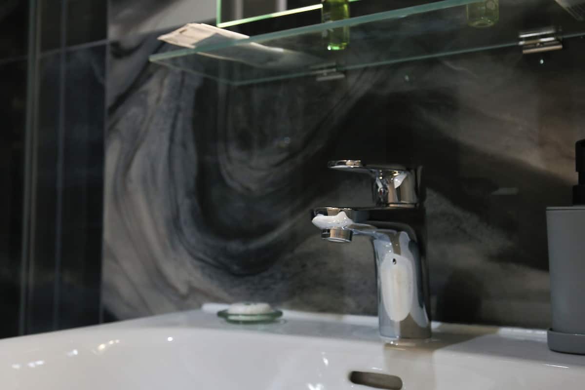 A bathroom with a glass shower enclosure, a white sink, and a marble wall.