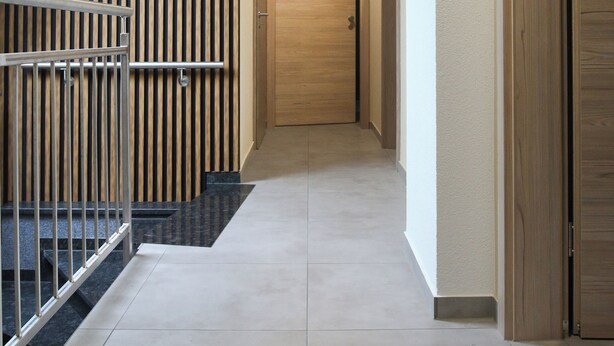 A modern hallway with a wooden staircase, a light fixture, and a door at the end. - Hotel Löwenstein (Lich)