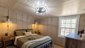 Een slaapkamer met een bed, nachtkastjes, een raam en een plafondventilator.
