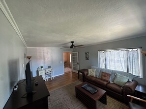 A living room with a brown leather sofa, a coffee table, a television, and a ceiling fan.