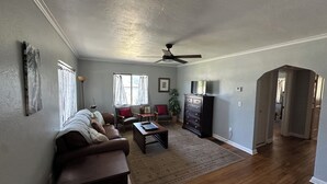 A spacious living room with a ceiling fan, a brown leather sofa, a coffee table, and a television on a dresser.