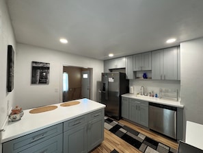 Una cocina moderna con armarios grises, un refrigerador de acero inoxidable, lavavajillas integrado y encimera blanca.
