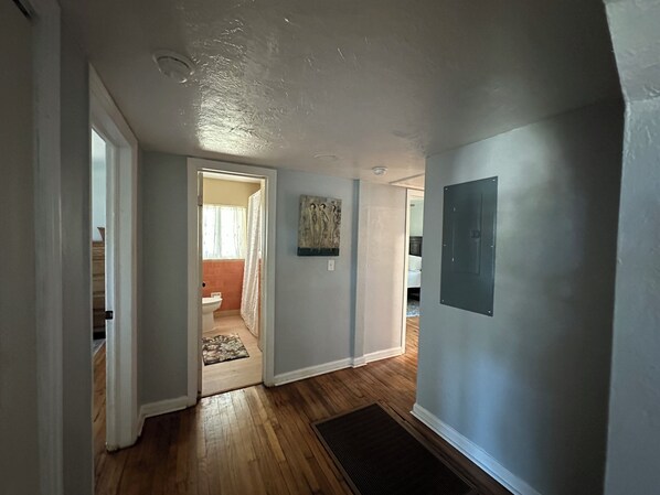 A hallway with wooden flooring, a door leading to a bathroom, and a wall-mounted light fixture.