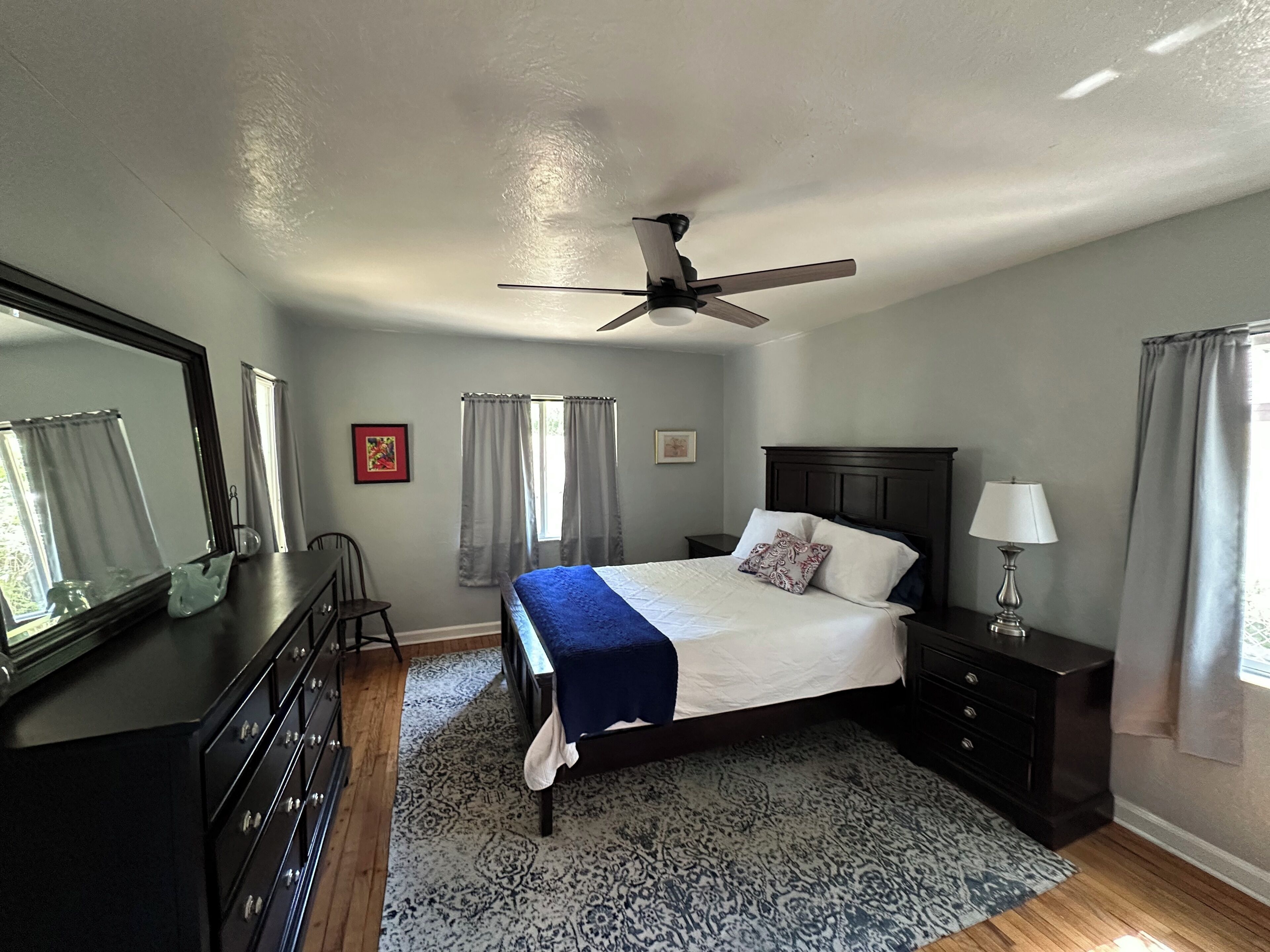 A bedroom with a bed, a ceiling fan, a dresser, a nightstand, and a lamp.