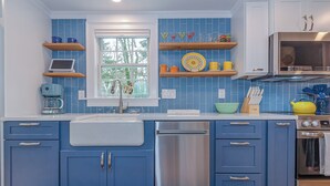 A kitchen with blue cabinets, a dishwasher, a microwave, and a window with a view of trees. - Charming 3-bedroom cottage with WiFi, AC in Rochester (Rochester)