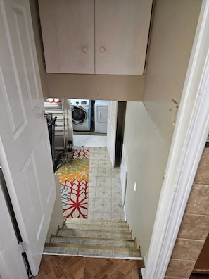 Stairs lead to a laundry area with a washing machine, dryer, and storage cabinet.