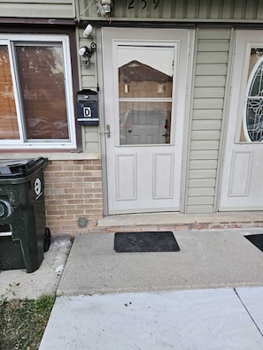 Stylish entrance with a white door, glass panel, and small window, accompanied by a black mailbox and trash bin.