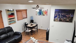 A living room with a black leather sofa, a dining table with chairs, a coffee table with a vase, a water dispenser, and a cityscape painting on the wall. - Charming 3-bedroom townhome in Pleasant Des Plaines with AC, WiFi (Des Plaines)