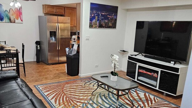 A modern living room with a black leather sofa, a glass coffee table, a patterned rug, a refrigerator, a TV, and a ceiling fan. - Charming 3-bedroom townhome in Pleasant Des Plaines with AC, WiFi (Des Plaines)