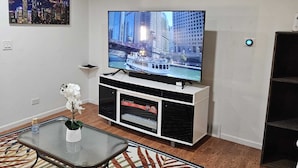 A living room with a flat-screen TV on a white entertainment unit, a glass coffee table, and a patterned rug. - Charming 3-bedroom townhome in Pleasant Des Plaines with AC, WiFi (Des Plaines)