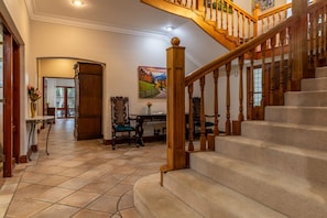 A spacious foyer with a wooden staircase, a large wooden cabinet, and a painting on the wall. - Selborne Golf Estate First Private Stays (Pennington)