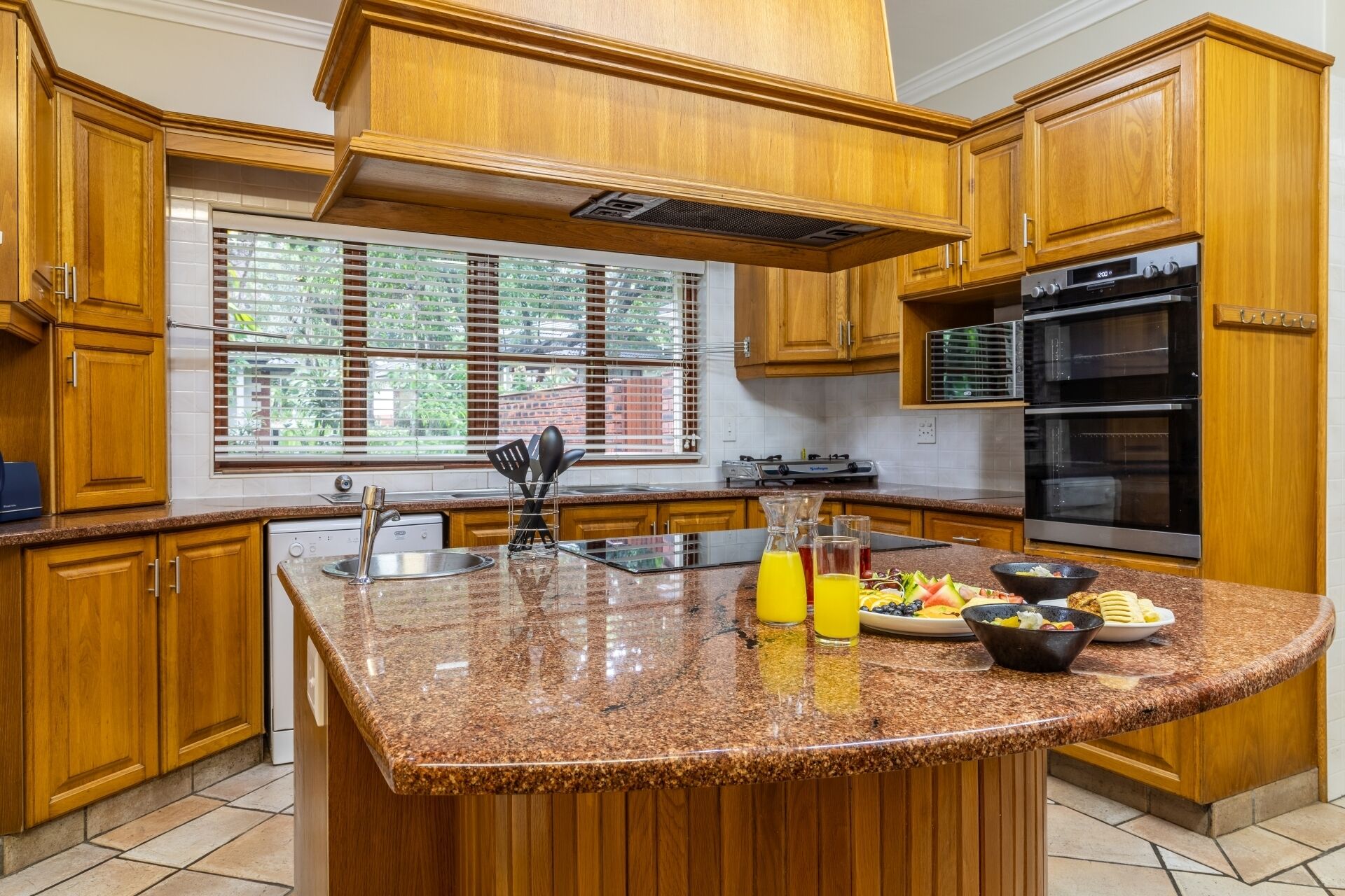 Una cocina con armarios de madera, encimera de granito, pileta de acero inoxidable, estufa y horno.