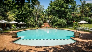 Ein Schwimmbecken, umgeben von Liegestühlen und Sonnenschirmen, mit einem Ziegelweg, der zu einer Treppe führt.