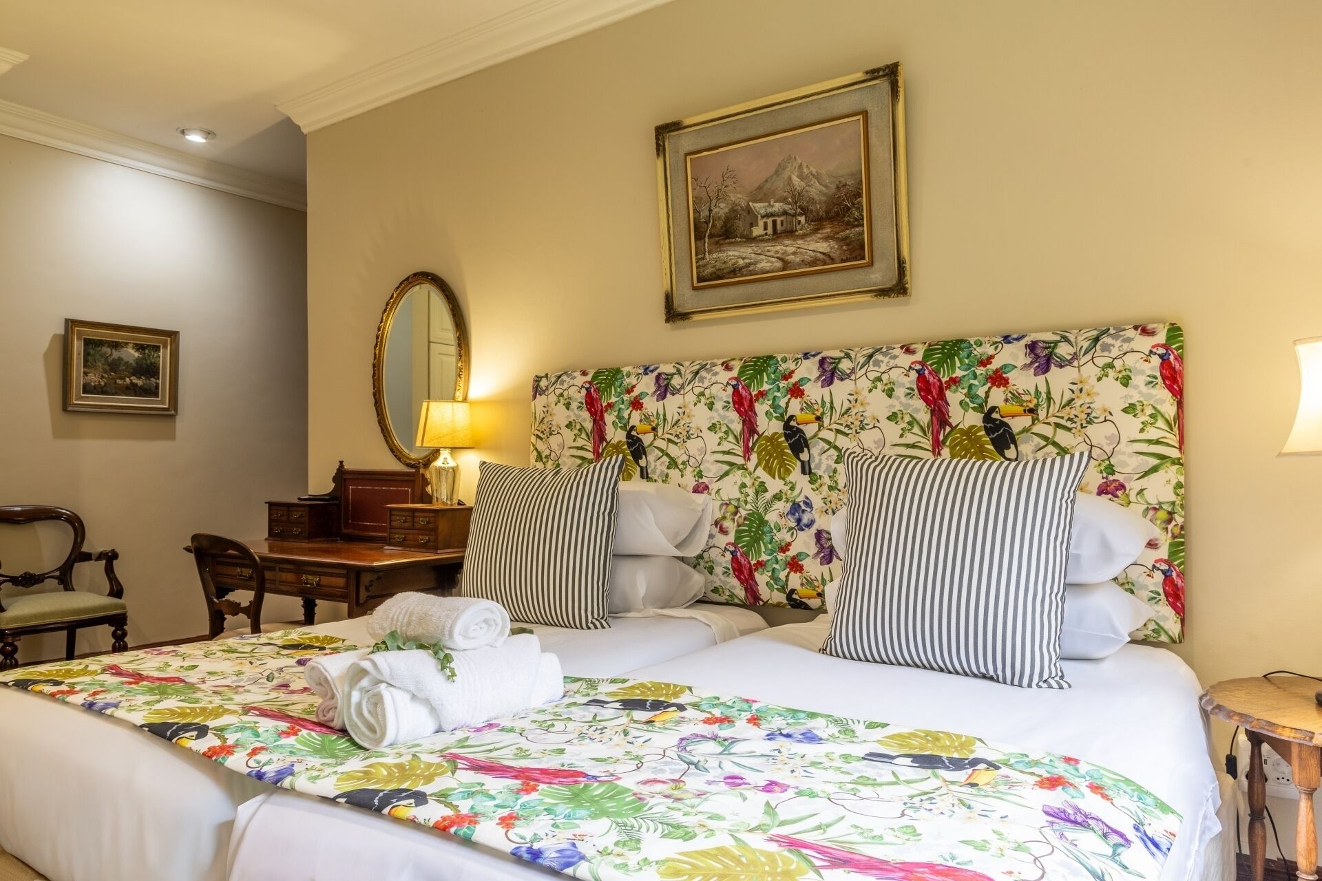 A hotel room with a large bed, two bedside tables, a desk, a chair, a mirror, and a painting on the wall.