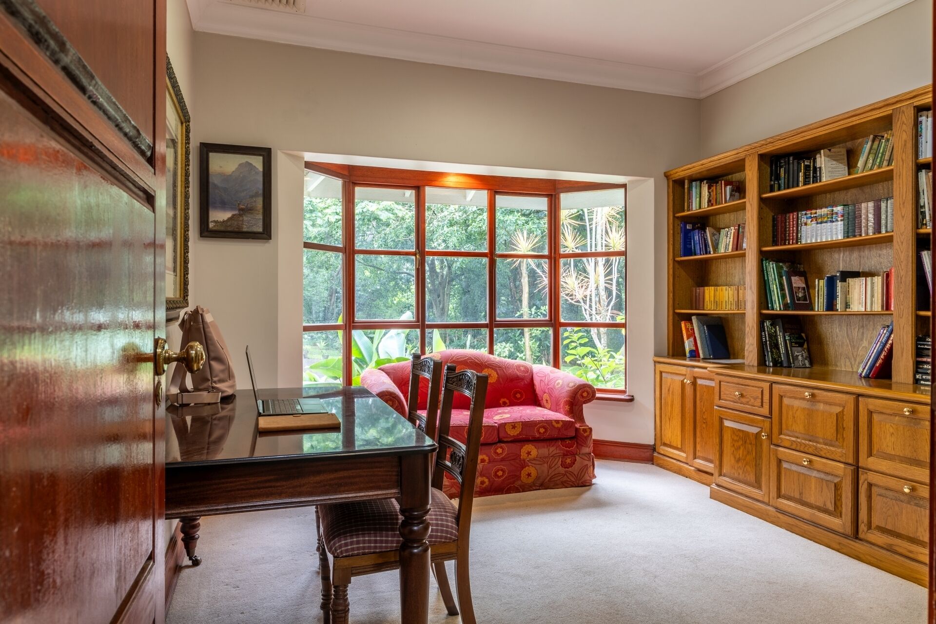 A room with a large window, a desk, a chair, and a bookshelf.
