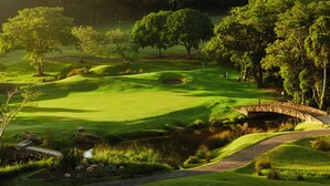 Ein Golfplatz mit einer Steinkreuzung, üppiger Vegetation und einem Teich.