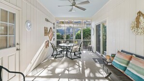 A sunlit patio with a round table and chairs, a ceiling fan, and a bench with cushions. - Serene Retreat on East Beach sleeps 6 guests (St Simons Island)