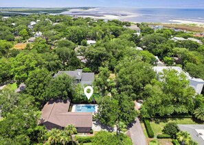 An aerial view of a residential area with a swimming pool, surrounded by dense greenery and houses.
