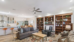 A modern living room with a sofa, coffee table, and a fireplace. There are bookshelves and a dining area in the background. - Serene Retreat on East Beach sleeps 6 guests (St Simons Island)