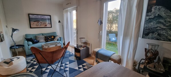A cozy living room with a blue sofa, a brown chair, and a patterned rug. There is a framed picture on the wall and a window with a view of the outdoors.