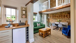 A spacious living area with a kitchen, a green sofa, a dining table with chairs, and a loft bedroom with a balcony. - Cherry Cottage Nr Grantley Hall (Grantley)
