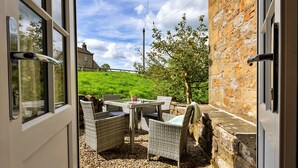 An open door leading to an outdoor patio with wicker furniture and a stone wall. - Cherry Cottage Nr Grantley Hall (Grantley)