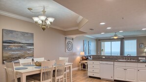 Una cocina amplia con armarios blancos, un comedor con mesa y sillas, y un gran ventanal con vistas al exterior.