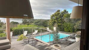 A wooden deck with a pool, lounge chairs, and a view of the sea.