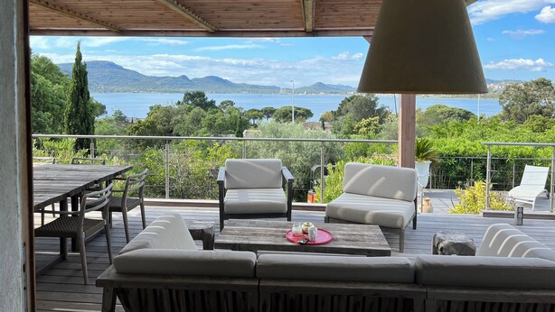 A wooden deck with outdoor seating, a hanging lamp, and a view of a lake and mountains.