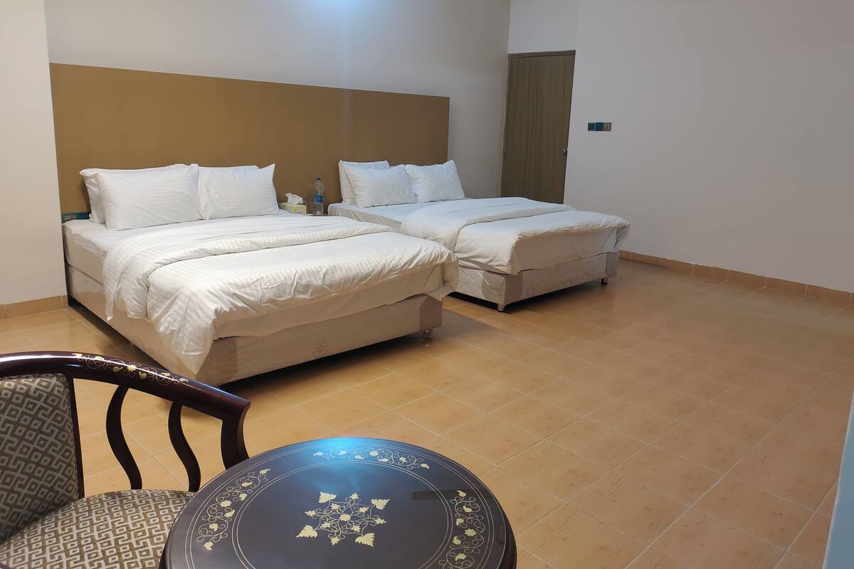 A hotel room with two beds, a wooden headboard, a round table, and a chair.