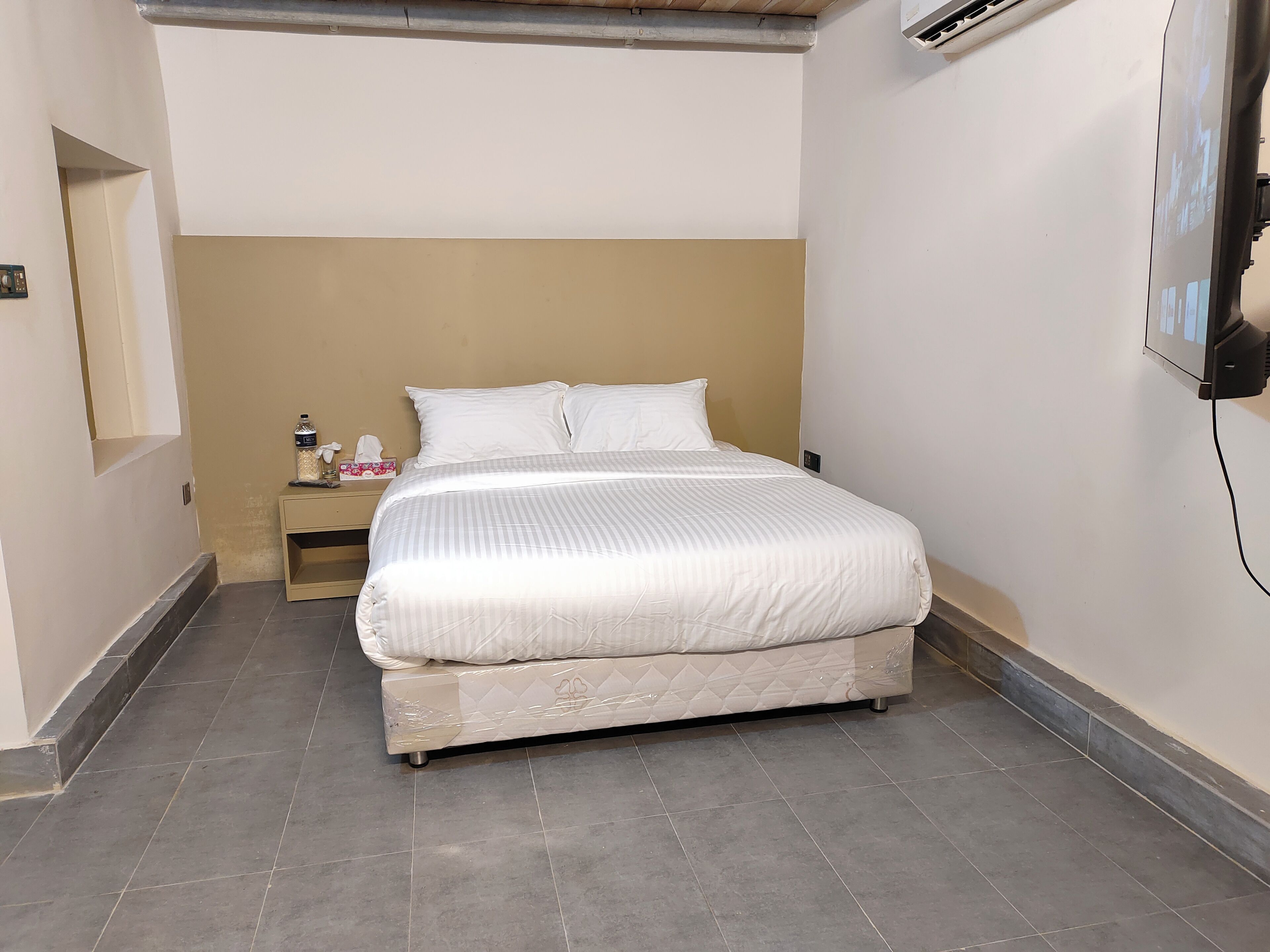 Een net opgemaakt bed in een hotelkamer, met een effen muur en een klein nachtkastje.