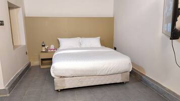 Een net opgemaakt bed in een hotelkamer, met een effen muur en een klein nachtkastje.