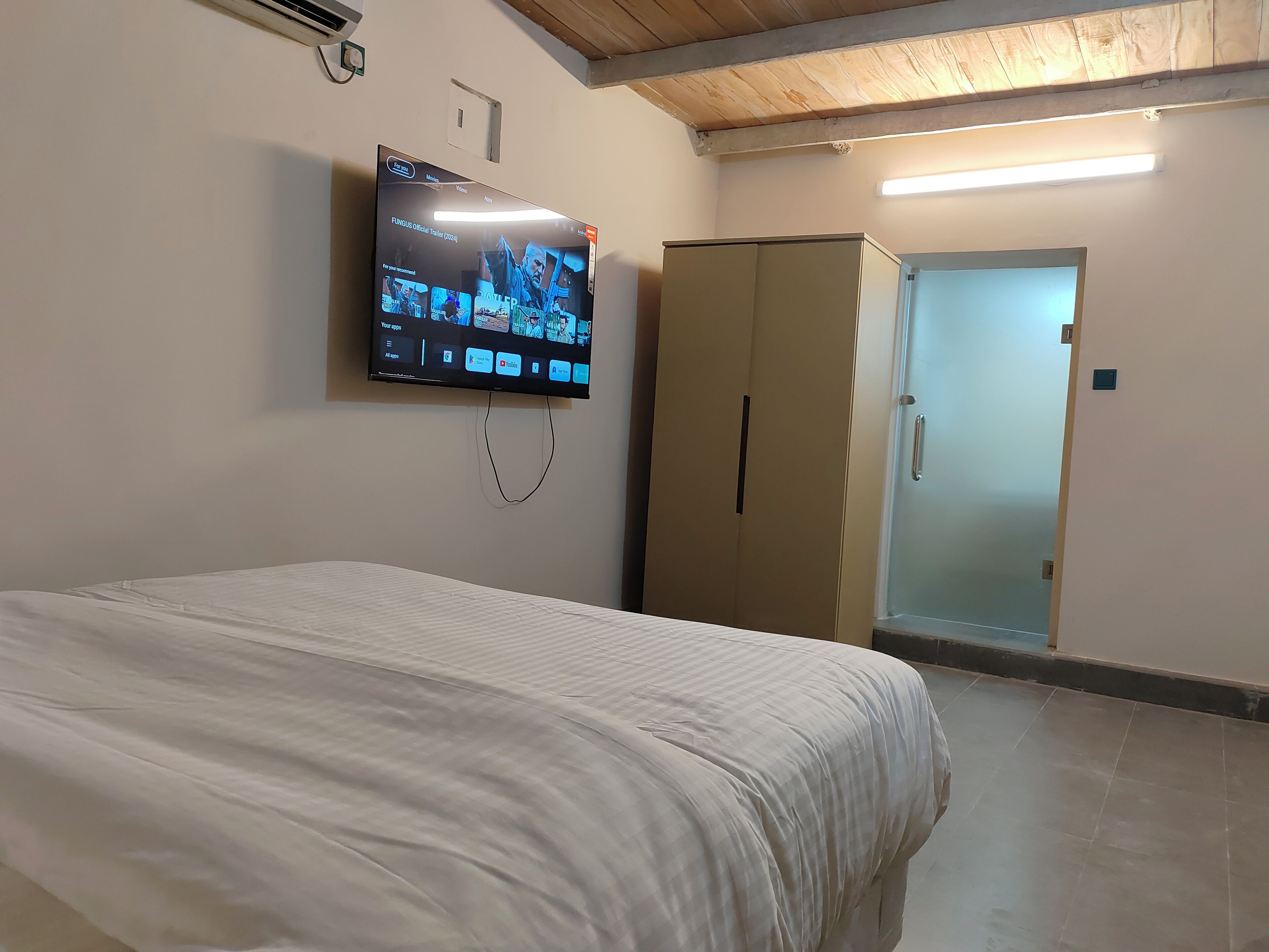 A hotel room with a bed, a TV mounted on the wall, a wardrobe, and a door.