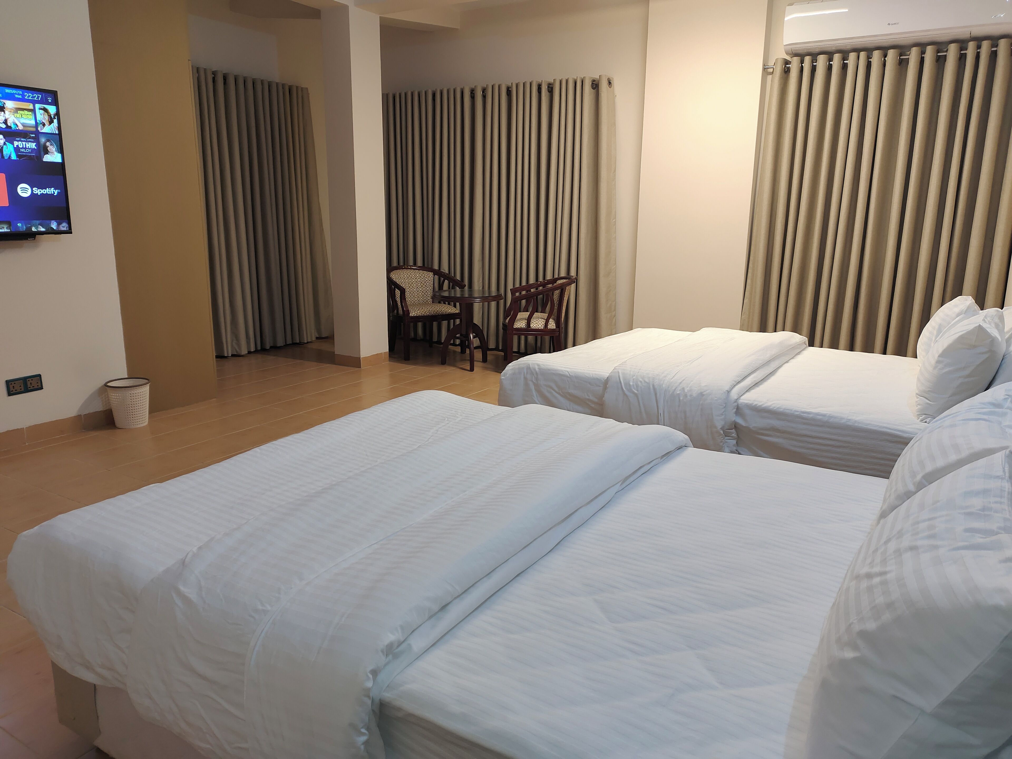 A hotel room with two beds, a TV, a chair, and a table.