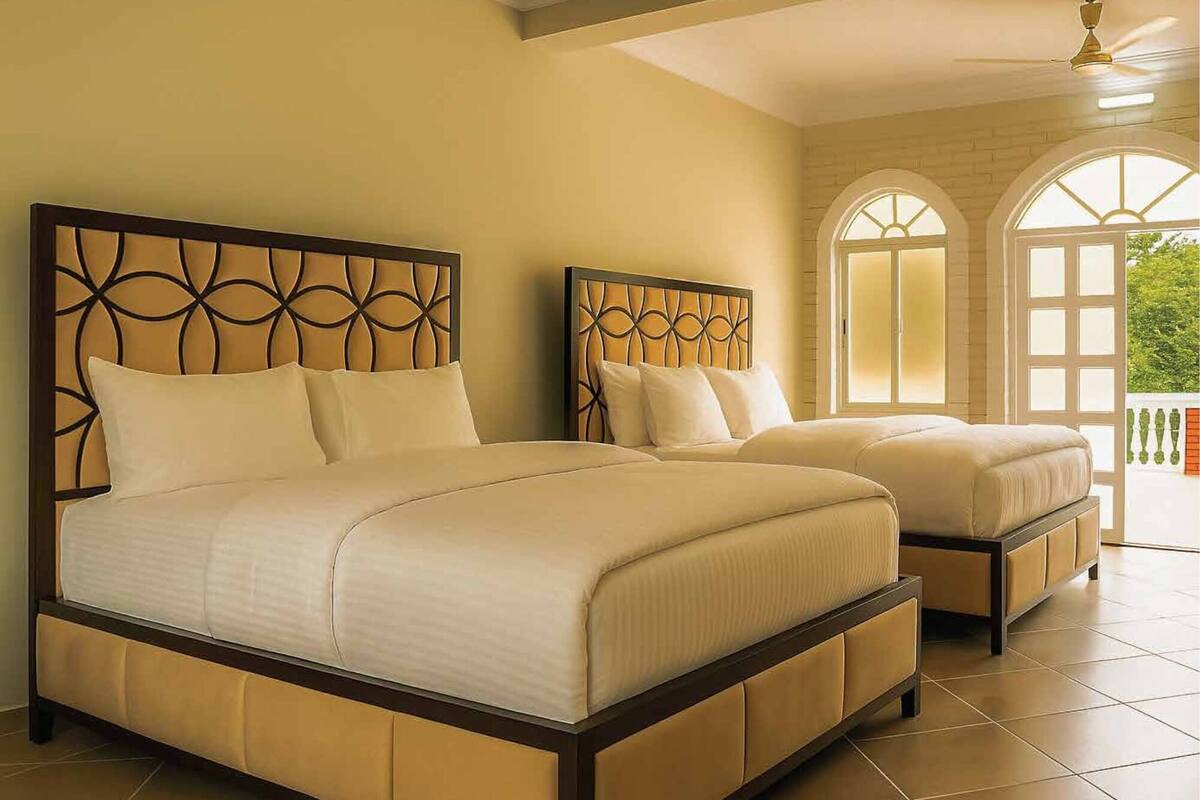 A hotel room with two beds, a balcony, and a view of greenery.
