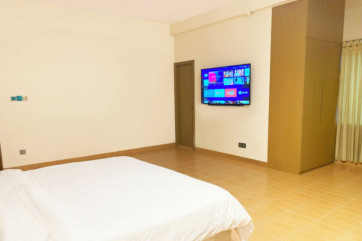 A hotel room with a large bed, a flat-screen TV mounted on the wall, and a door leading to another room.
